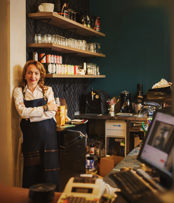 A smiling female shop owner standing proudly in her well-stocked, successful high street store.